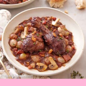Pinterest graphic of coq au vin in a plate with torn bread in the back along with a second plate.