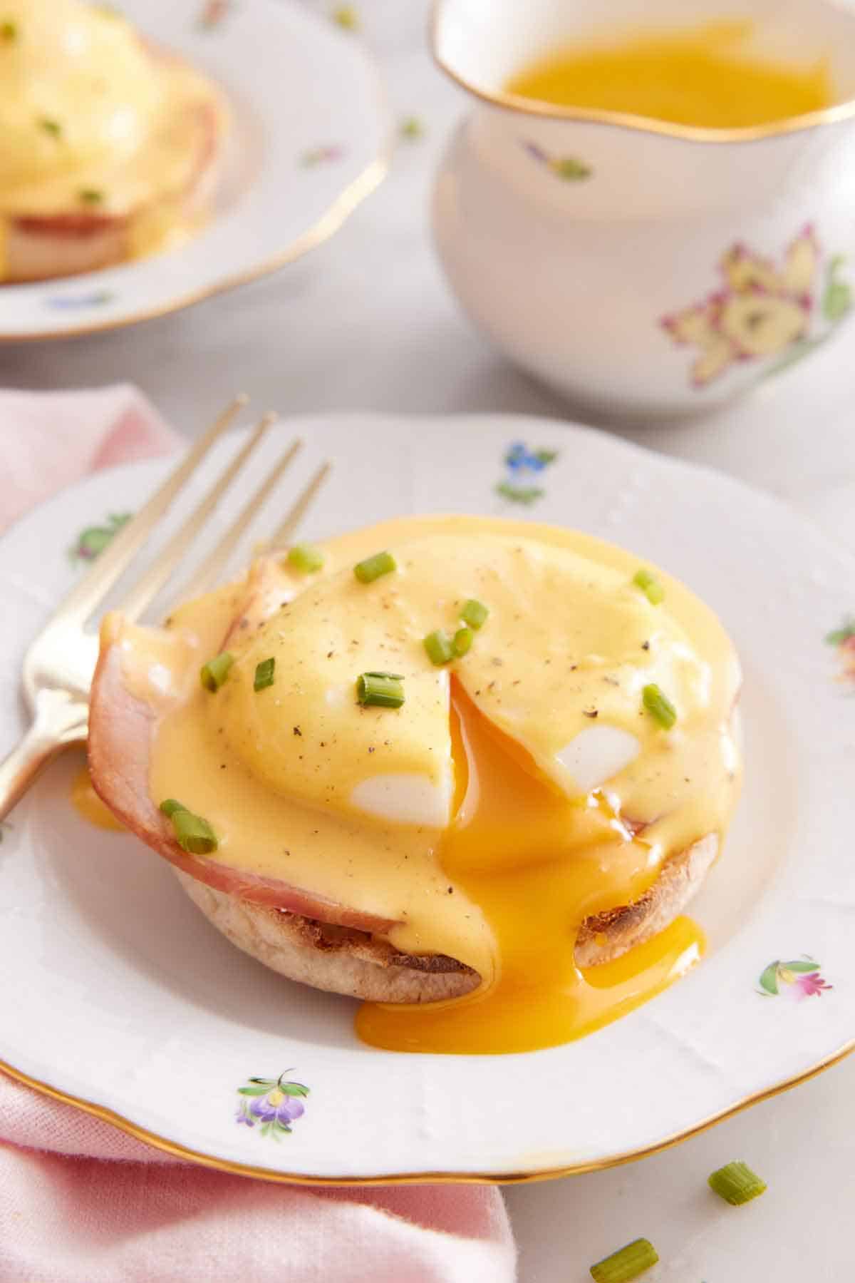 A plate with eggs benedict topped with sauce, cut open with the yolk running out.
