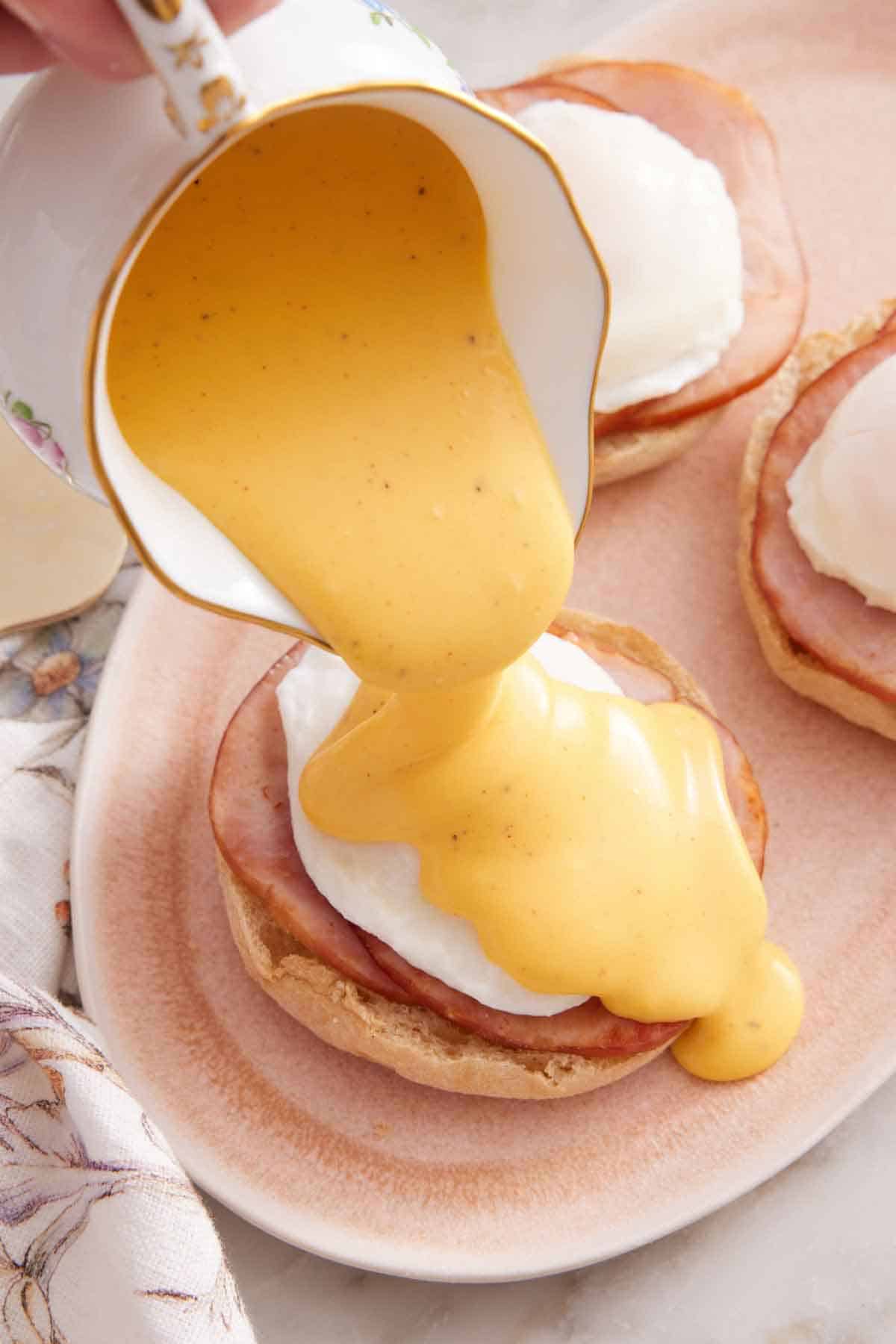 Hollandaise sauce poured over eggs benedict on a platter.