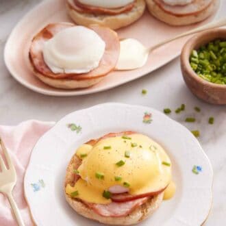Pinterest graphic of a plate with eggs benedict with hollandaise sauce over top with some chives. More eggs benedicts in the background.