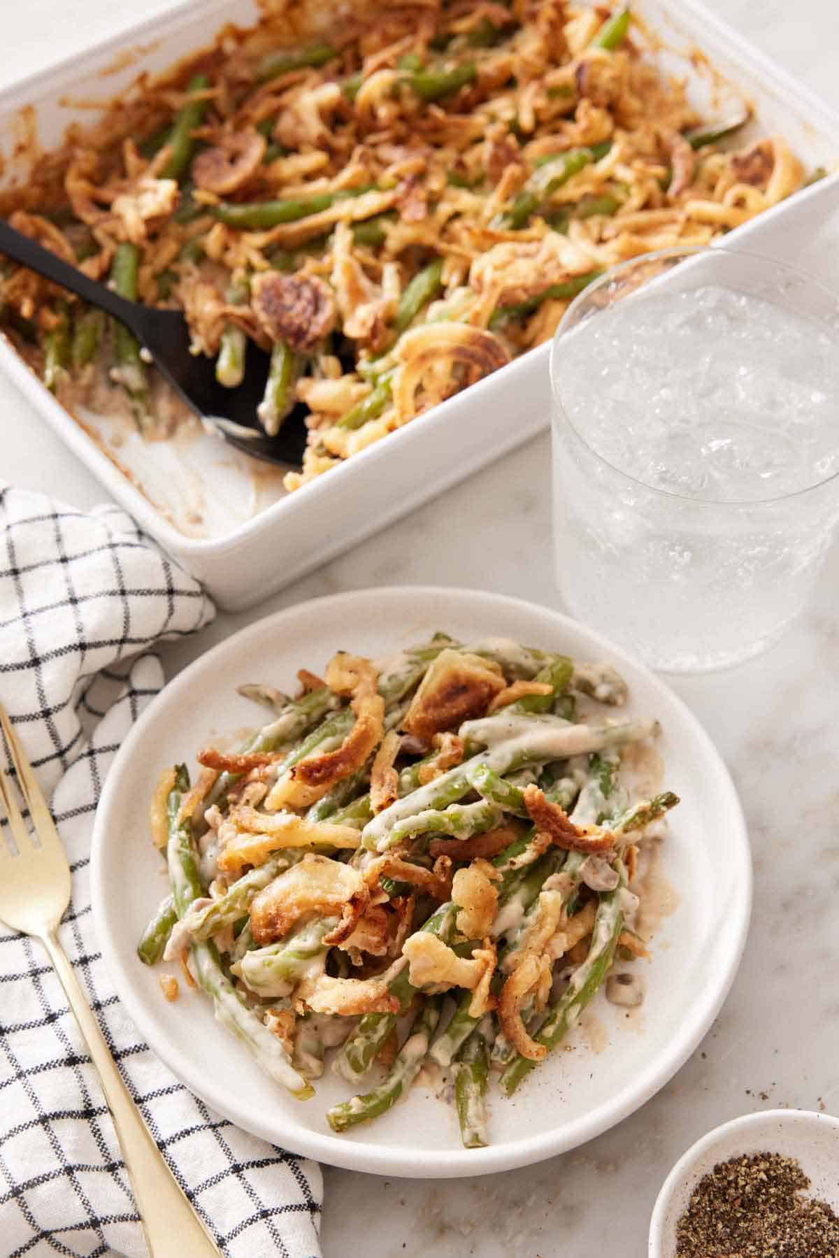 A plate with a serving of green bean casserole with a glass of water and baking dish in the background.