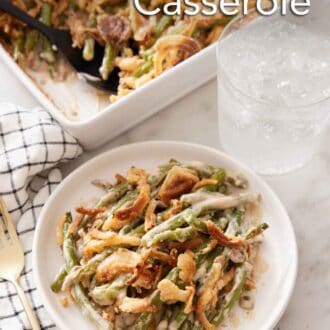 Pinterest graphic of a plate with a serving of green bean casserole with a glass of water and baking dish in the background.