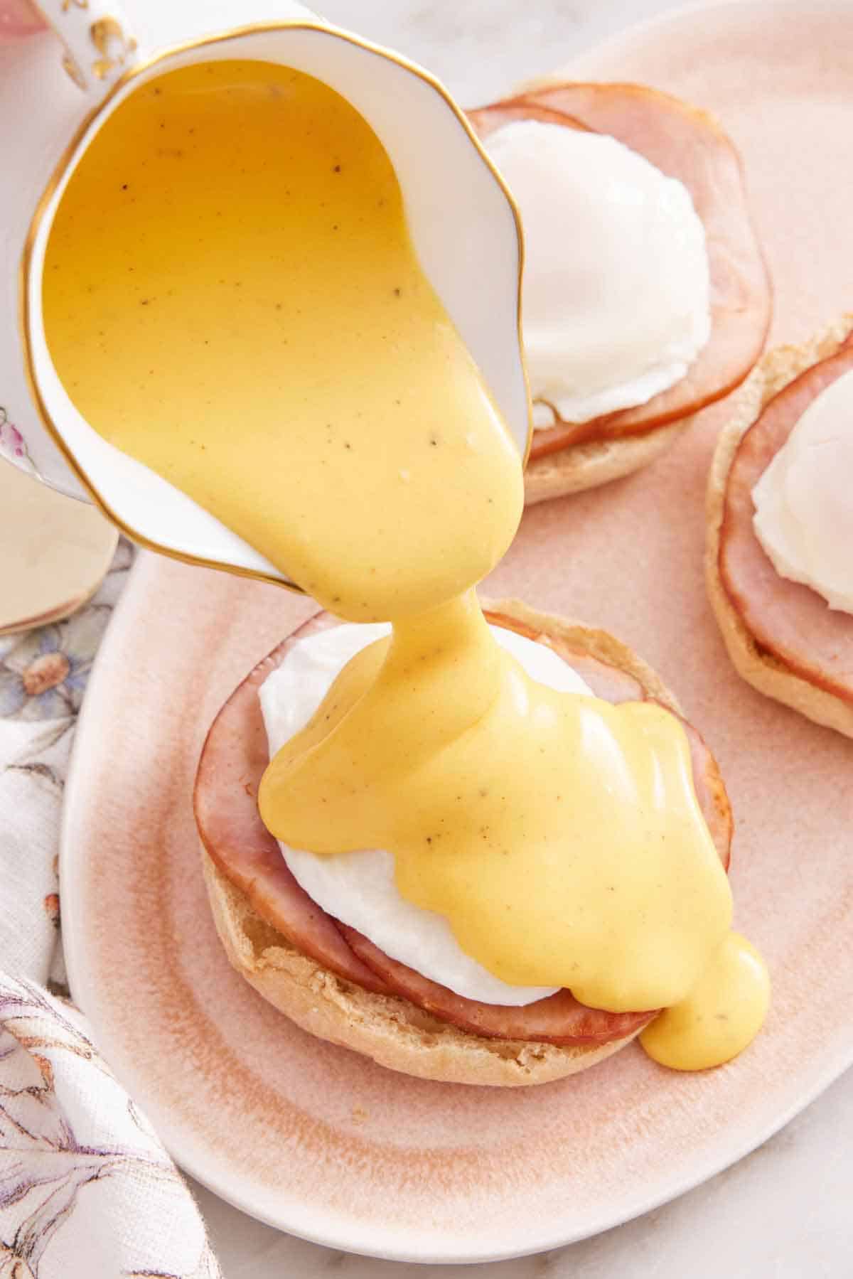A small pitcher of hollandaise sauce poured over eggs benedict.