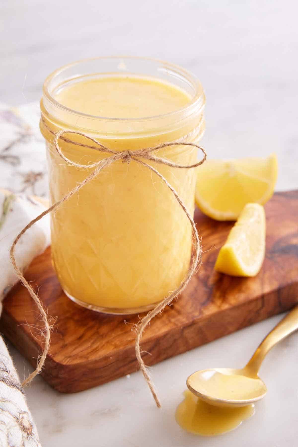 A mason jar of hollandaise sauce with a bow tied on it with some lemon wedges beside it.