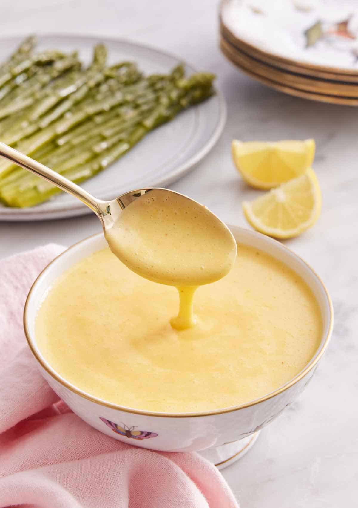 A bowl of hollandaise sauce with a spoonful lifted up with the sauce drizzling off.