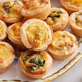 A platter of mini quiche with varying filling ingredients.