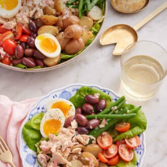 Pinterest graphic of a plate of niçoise salad with a glass of wine in the back with a platter with the rest of the salad.