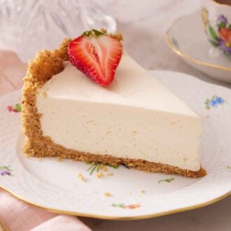 A slice of no bake cheesecake with a cut piece of strawberry on top on a plate.