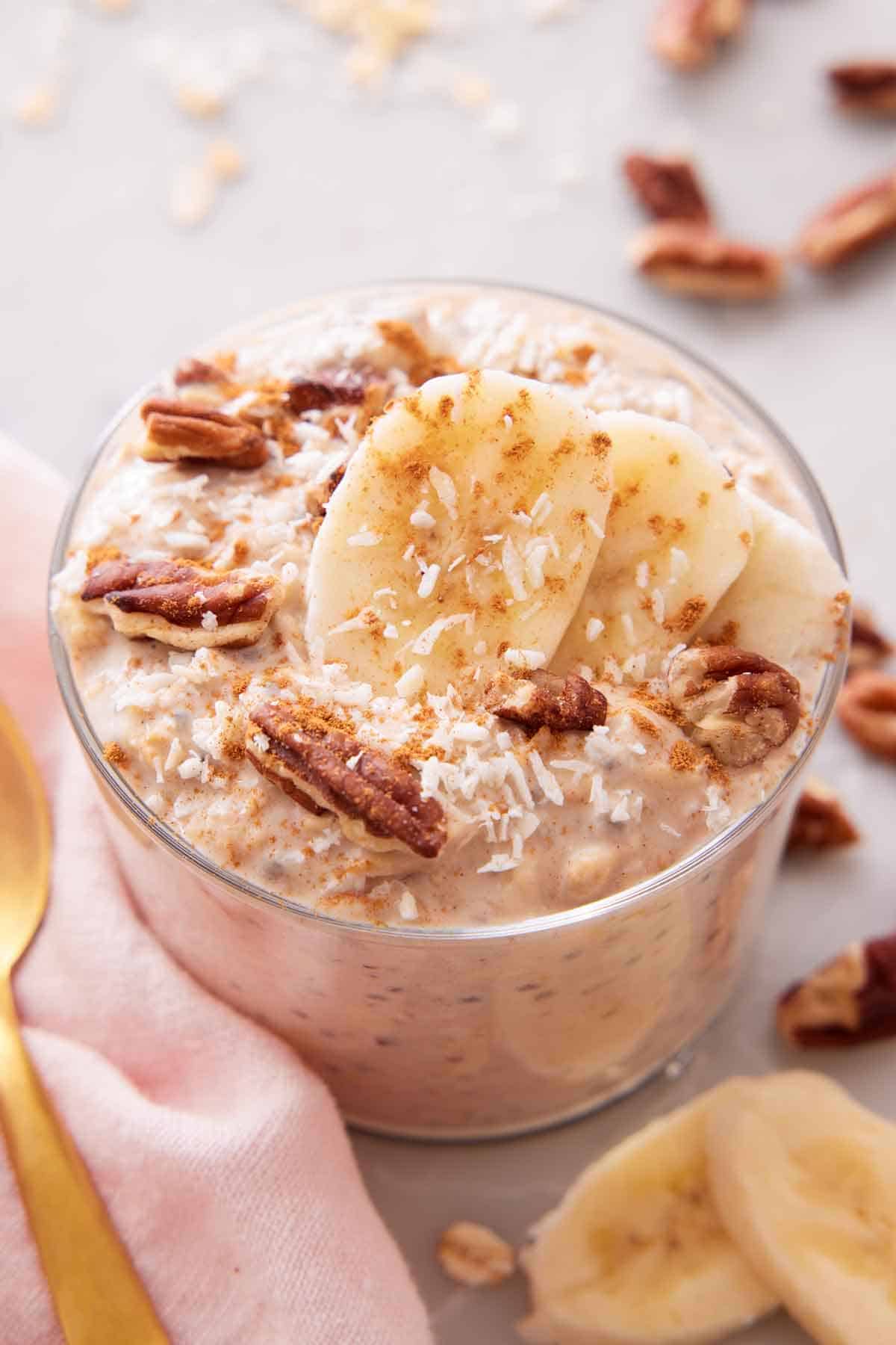 A jar of overnight oats topped with bananas, pecans, and shredded coconut.