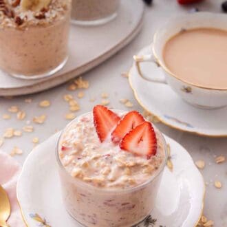 Pinterest graphic of a plate with a glass of overnight oats topped with strawberries with a cup of coffee and more overnight oats in the background.