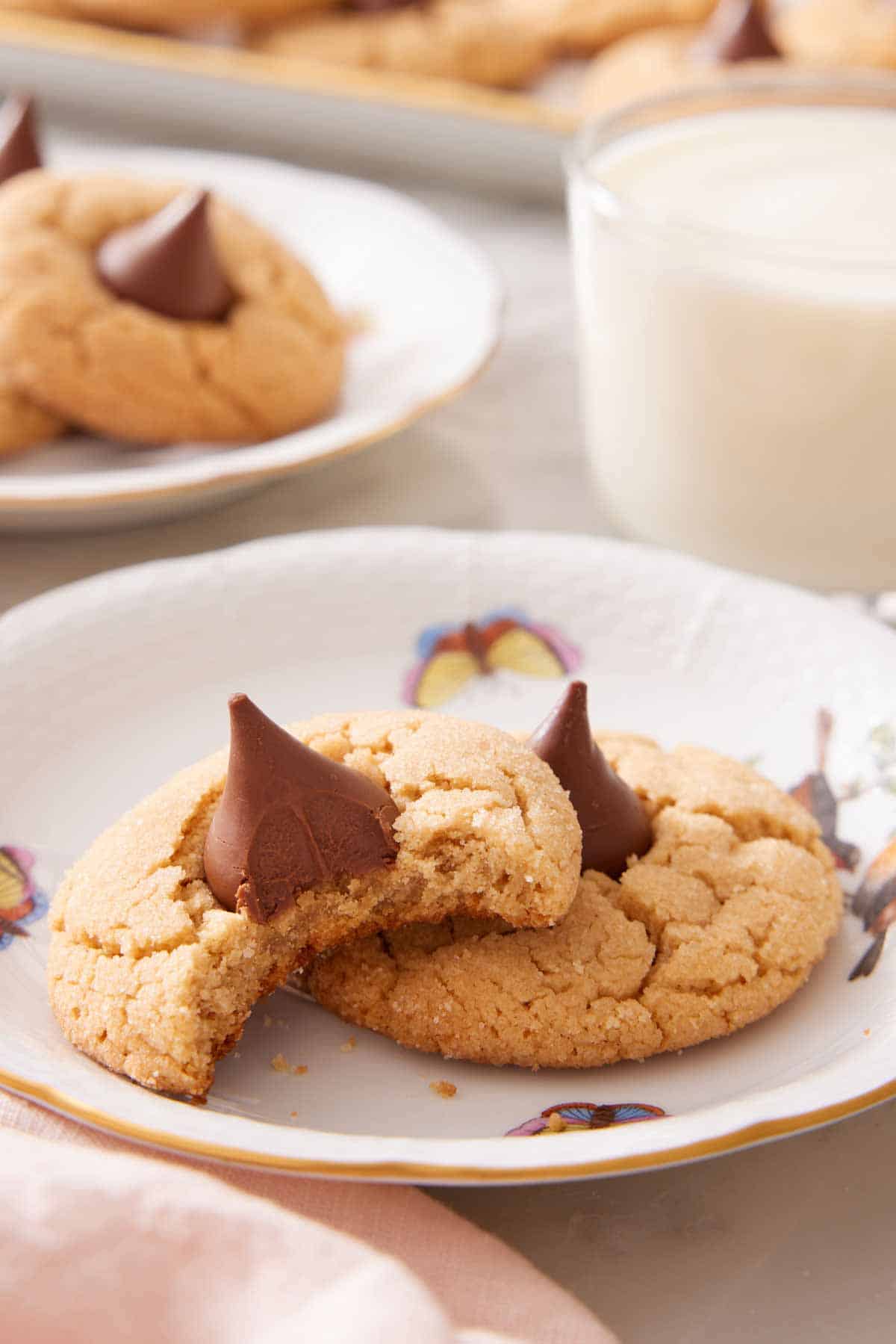 A plate with two peanut butter blossoms. One has a bite taken out of it.
