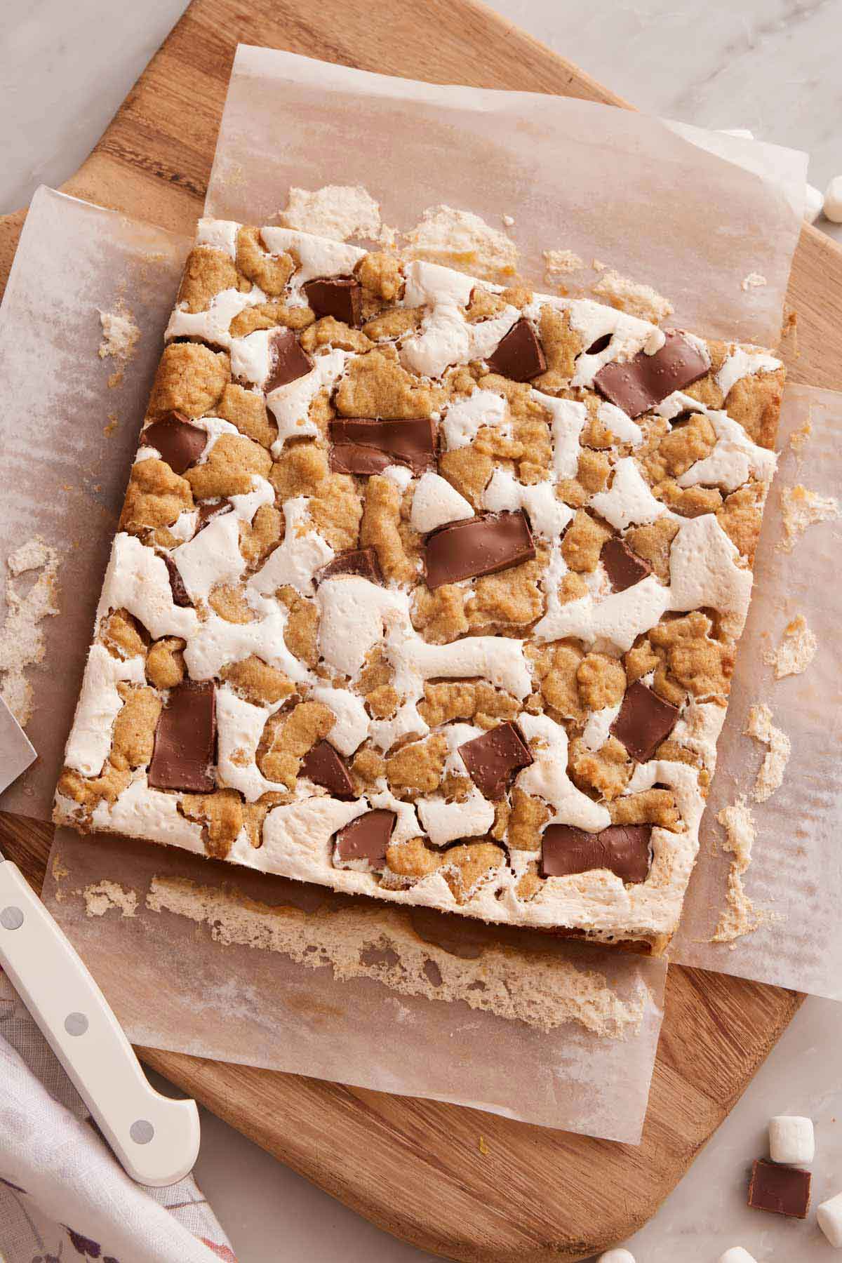 Overhead view of an uncut s'mores bars over parchment paper on a wooden serving board.