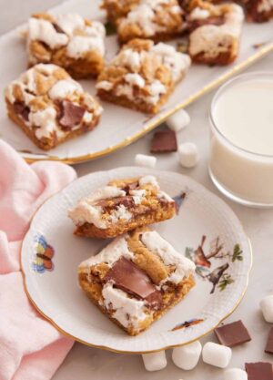 A plate with two pieces of s'mores bars with a cup of milk and platter of bars in the background.