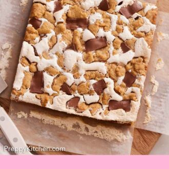 Pinterest graphic of an overhead view of an uncut s'mores bars over parchment paper on a wooden serving board.