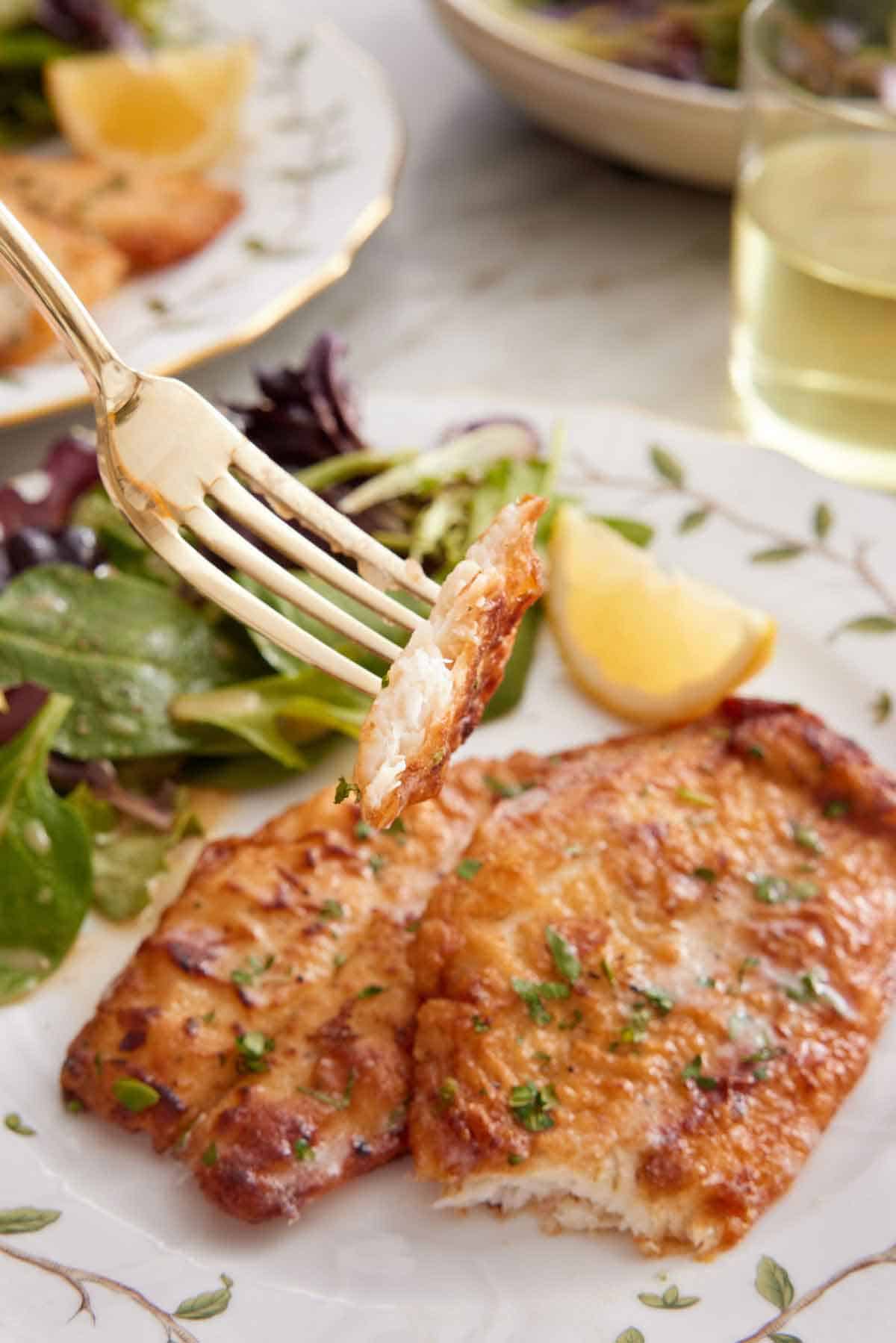 A fork lifting up a bite of sole meunière from a plate.