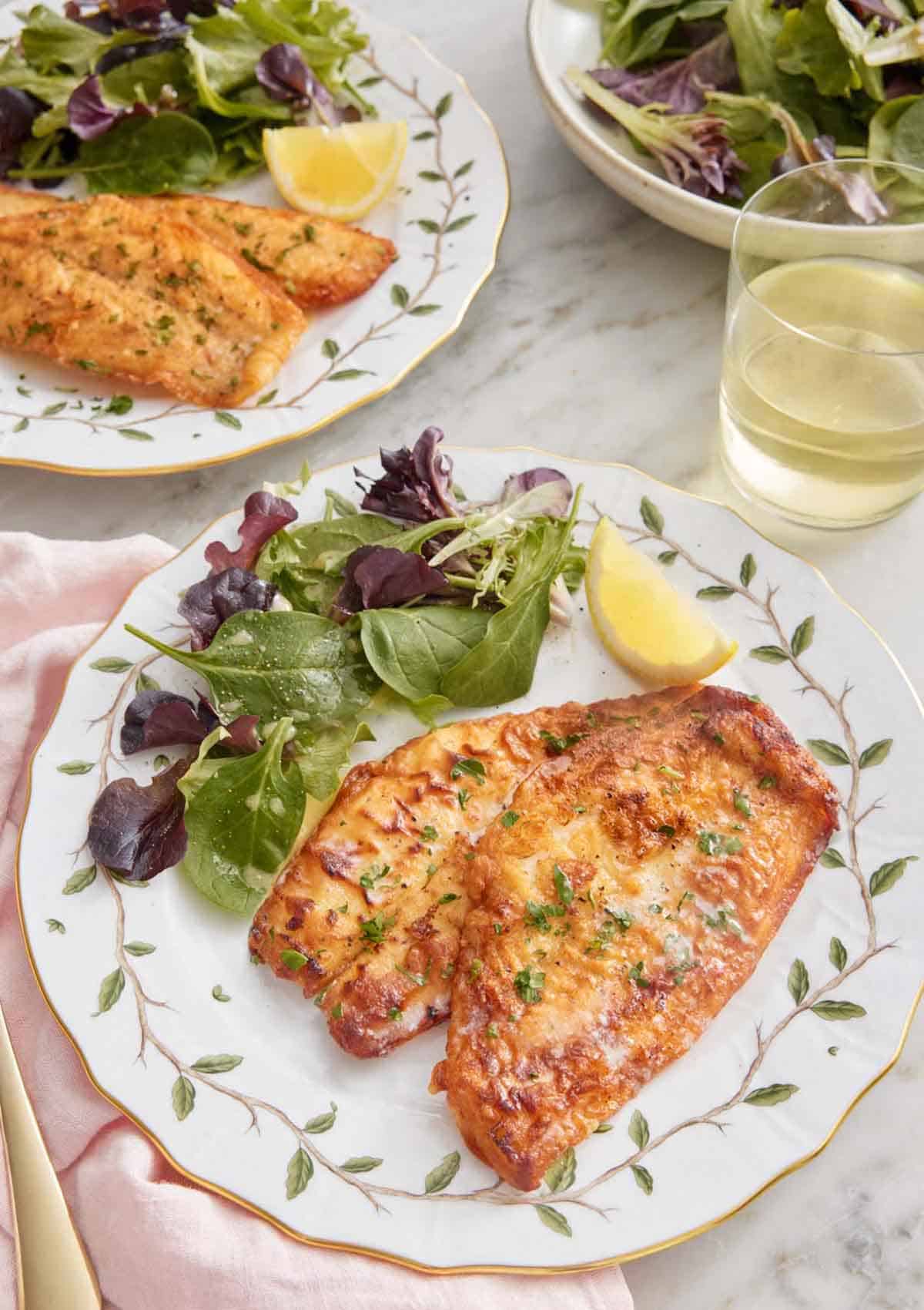 Two plates of sole meunière with a handful of mixed greens and a lemon wedge.