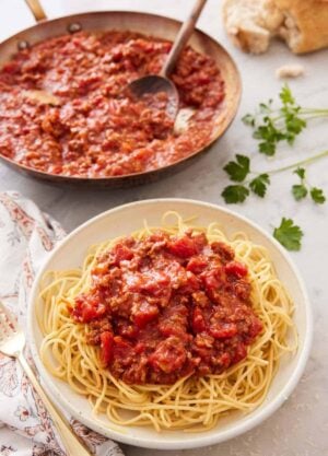 A bowl of noodles with spaghetti sauce on top with a skillet full of sauce in the background.