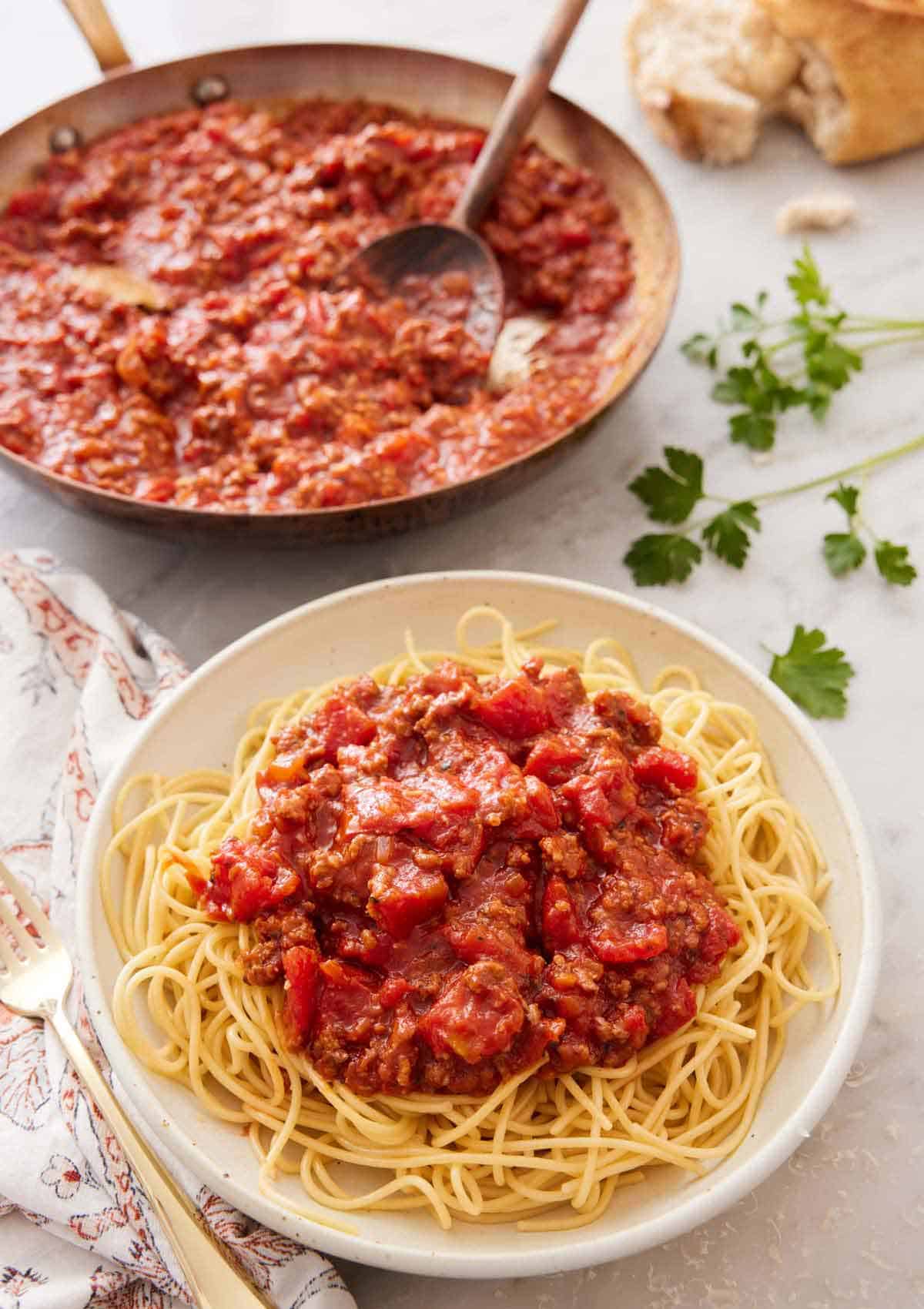 A bowl of noodles with spaghetti sauce on top with a skillet full of sauce in the background.
