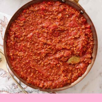 Pinterest graphic of an overhead view of a skillet of spaghetti sauce with a bay leaf and spoon inside.