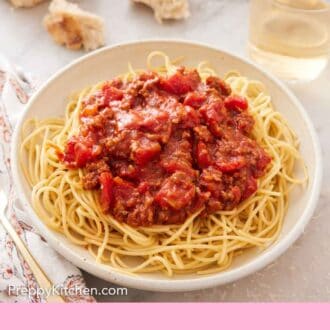 Pinterest graphic of a bowl of noodles with spaghetti sauce on top with torn bread and glass of wine in the background.