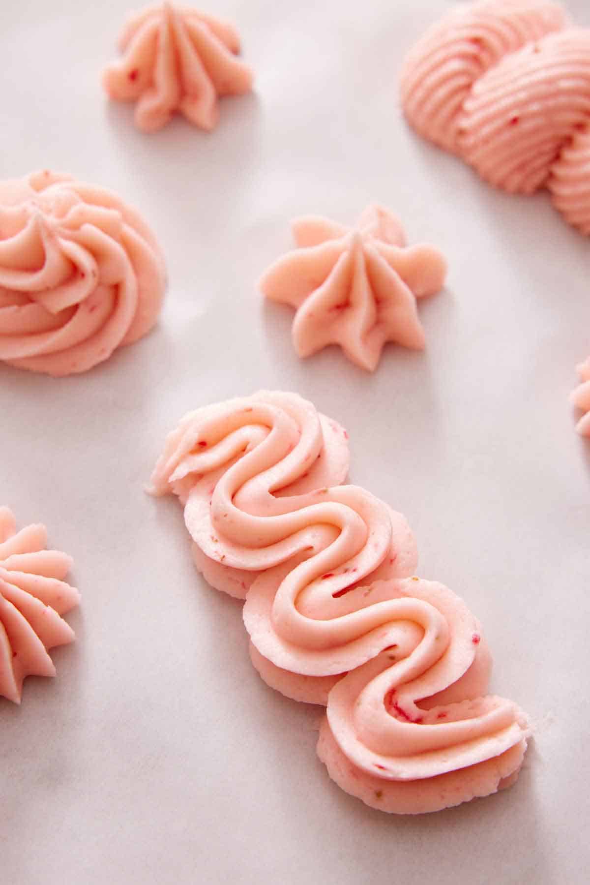 Strawberry frosting piped in different shapes on a flat surface.