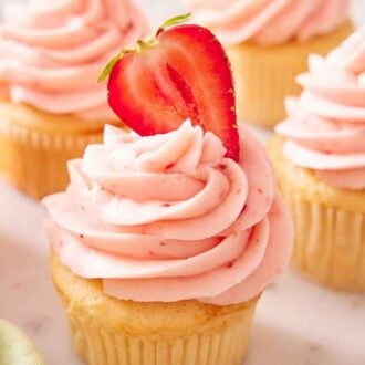 Cupcakes with strawberry frosting piped on top with one topped with a fresh cut strawberry.