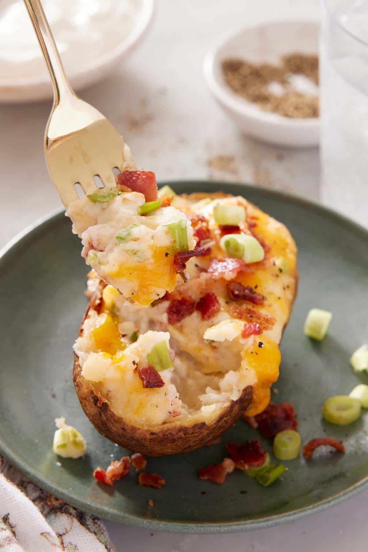 A forkful lifting up a bite of twice-baked potato on a plate.
