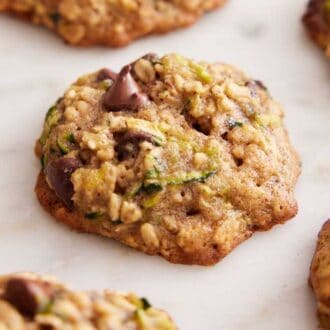 A zucchini cookie in focus with additional cookies off to the side.