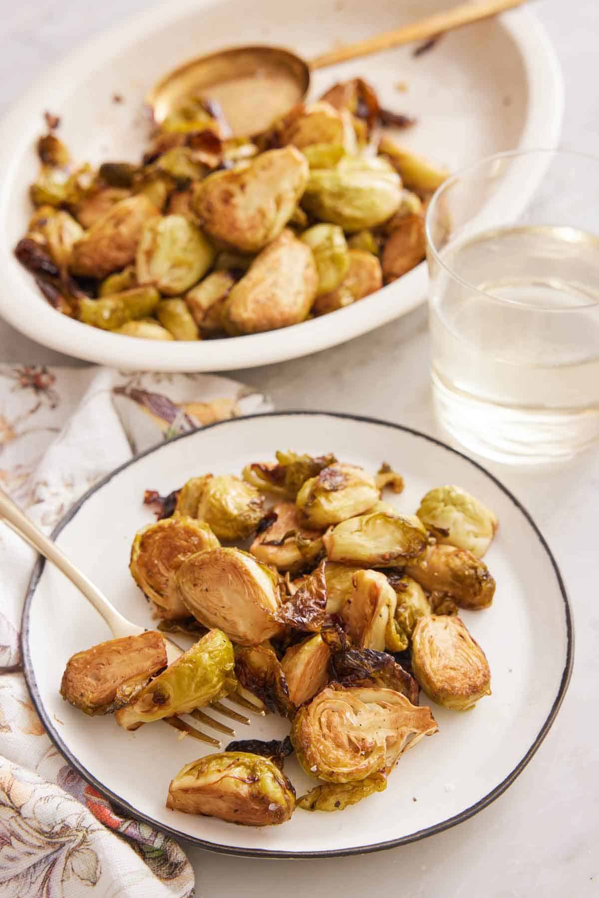 A plate of air fryer Brussels sprouts with a fork with a platter and drink in the background.