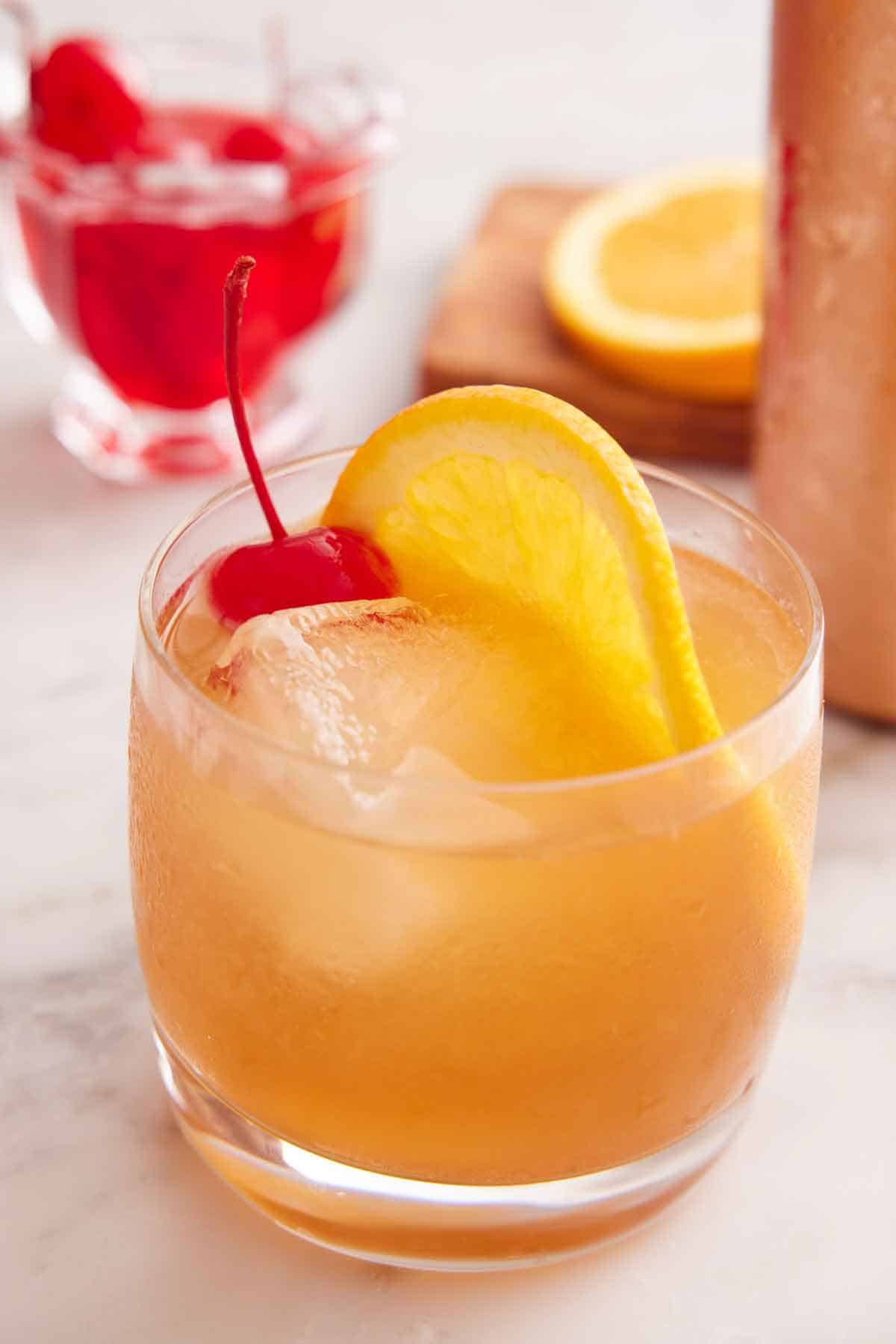 A glass of Amaretto Sour with a slice of orange and maraschino cherry.