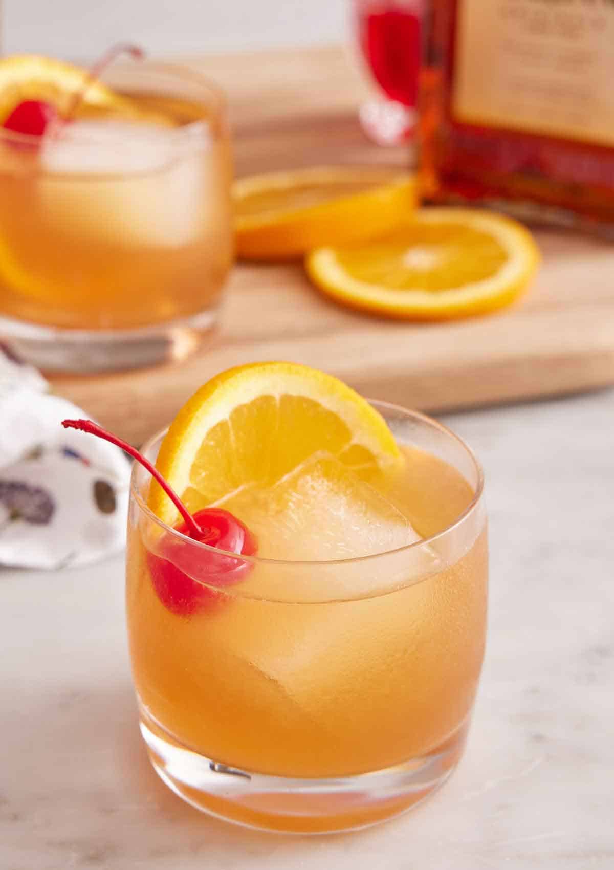 A glass of Amaretto Sour with a second one in the background along with orange slices.