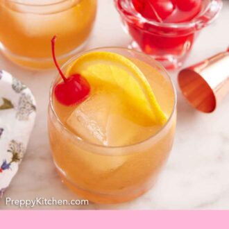 Pinterest graphic of two glasses of Amaretto Sour garnished with orange slices and maraschino cherries with a jar of more cherries in the back.