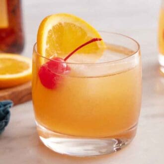 A glass of Amaretto Sour with a slice of orange and a maraschino cherry.