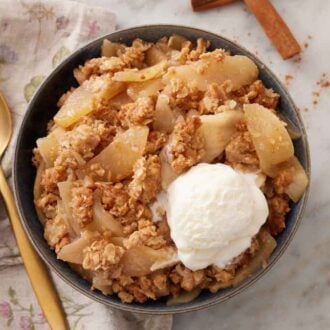 Overhead view of a bowl of apple crisp with a scoop of ice cream with a spoon beside it.