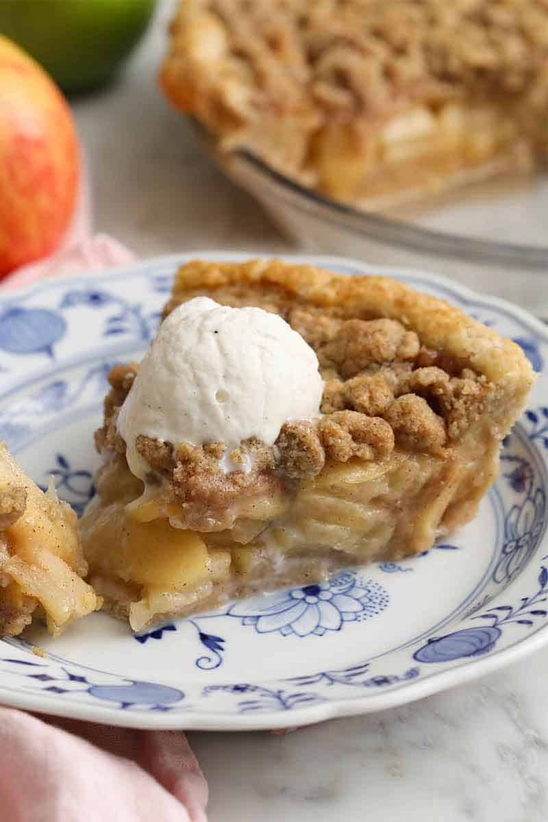 A close view of a slice of apple crumble pie on a plate with a scoop of ice cream on top.
