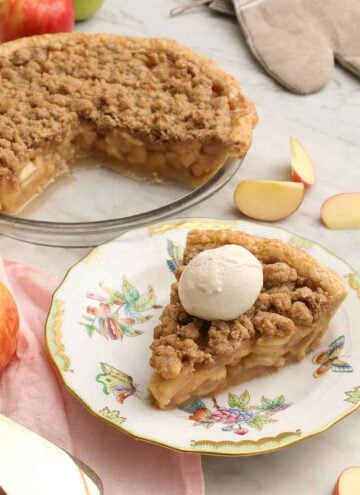 A plate with a slice of apple crumble pie with ice cream on top and the cut pie in the background.