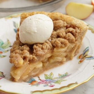 A slice of apple crumble pie on a plate with a scoop of ice cream on top.