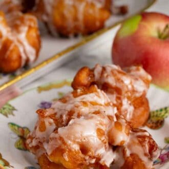 Pinterest graphic of a plate with apple fritters topped with glaze with an apple and platter of more fritters in the background.