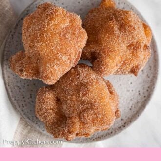 Pinterest graphic of an overhead view of a plate with three apple fritters coated in cinnamon sugar.