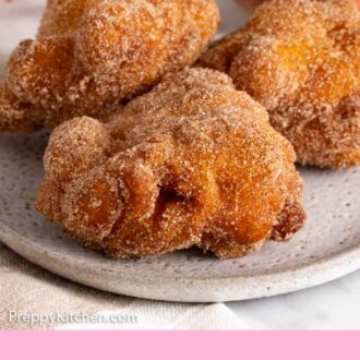 Pinterest graphic of an angled view of a plate with three apple fritters coated in cinnamon sugar.