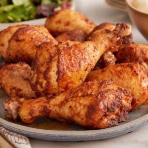 A platter of baked chicken legs with sides in the background.