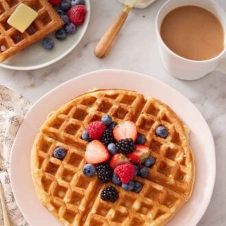 Pinterest graphic of a plate with a Belgian waffle topped with berries. Coffee, butter, and more waffles in the background.
