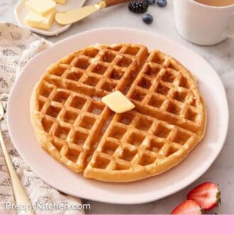 Pinterest graphic of a plate with a large Belgian waffle topped with butter. Coffee, berries, and butter in the background.