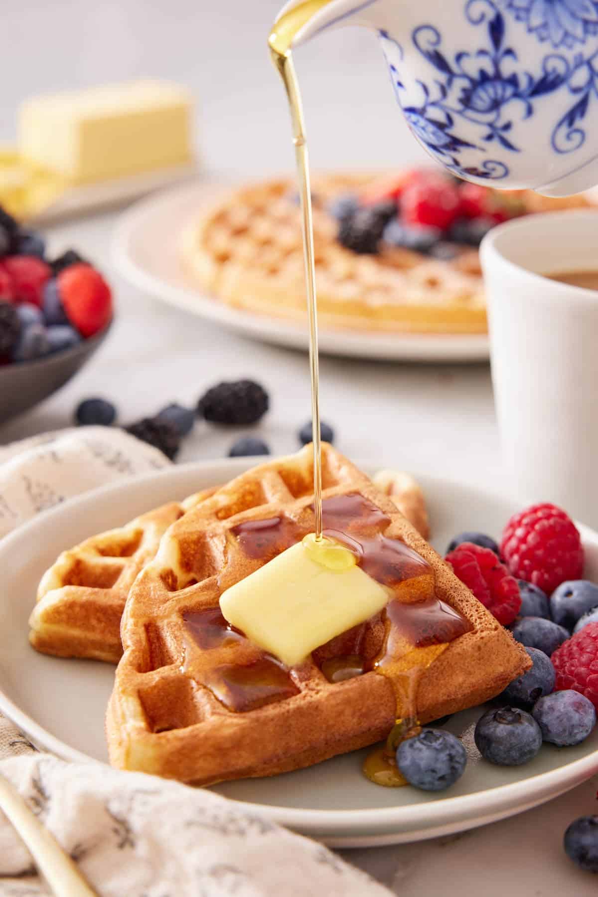Syrup poured over Belgian waffles with butter and fruit.