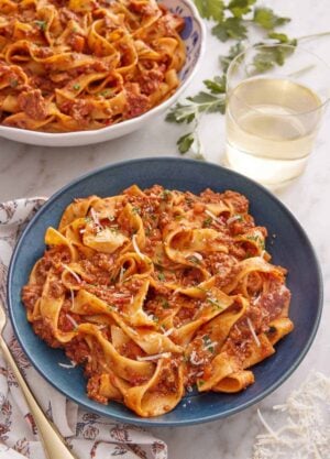 A bowl of bolognese with a glass of wine and a second bowl in the background.