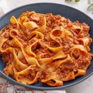 A bowl of bolognese with utensils on the side and parsley.