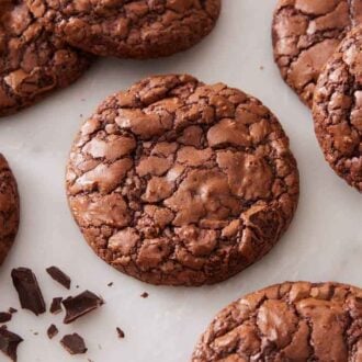 Brownie cookies on a marble surface with chopped chocolate scattered.