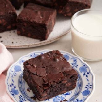 Pinterest graphic of a plate with a piece of brownie with a cup of milk and platter of brownies in the background.