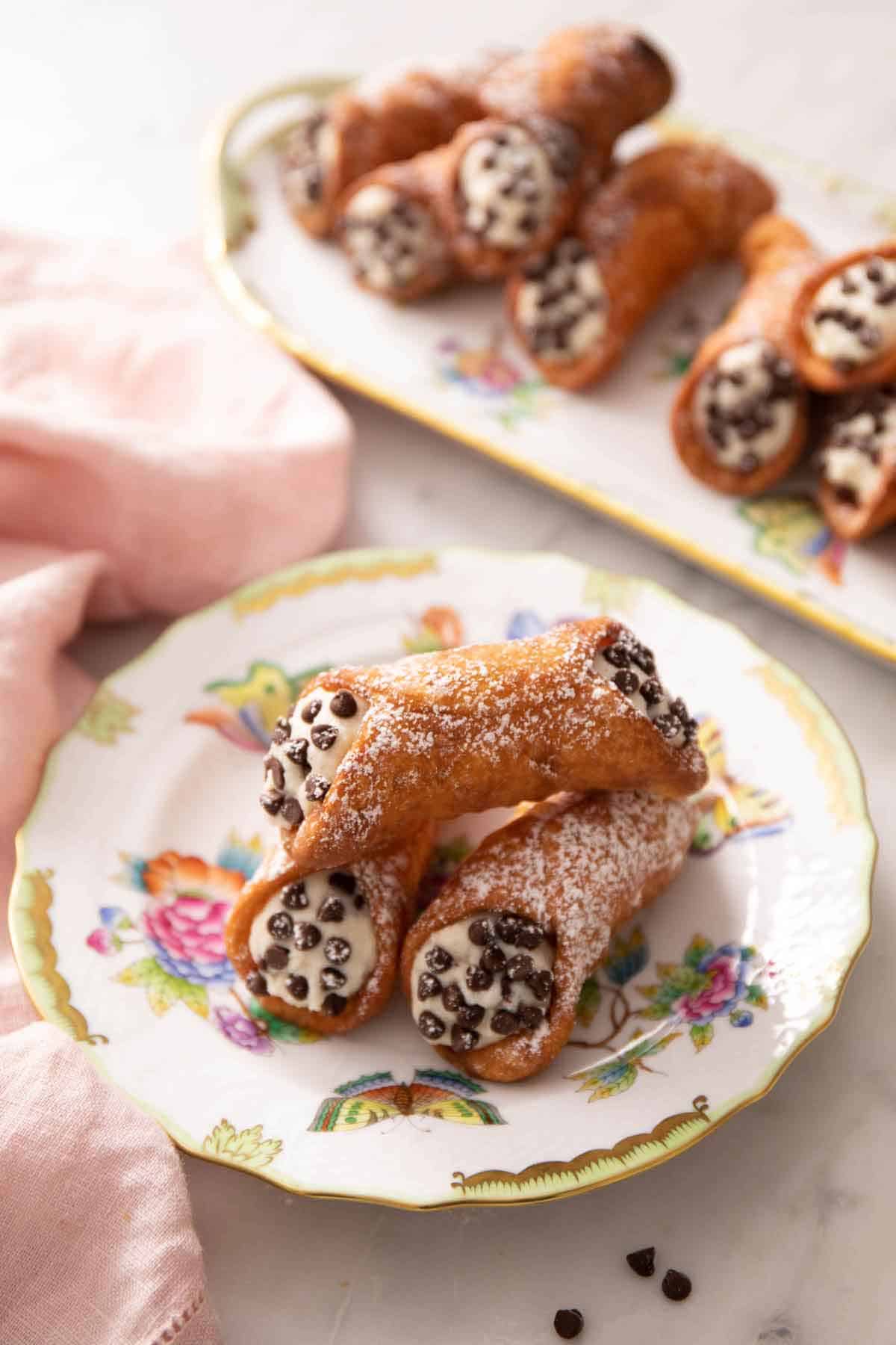 A plate with three cannoli with a platter in the background.