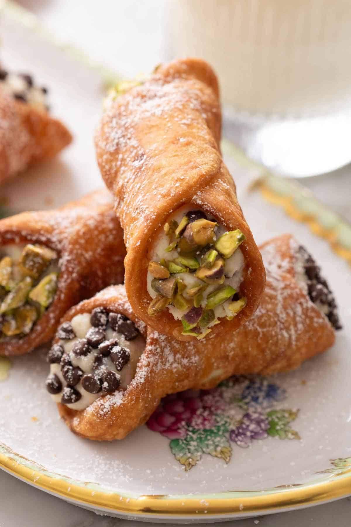 A stack of cannoli with crushed pistachos in two and chocolate chips in another.